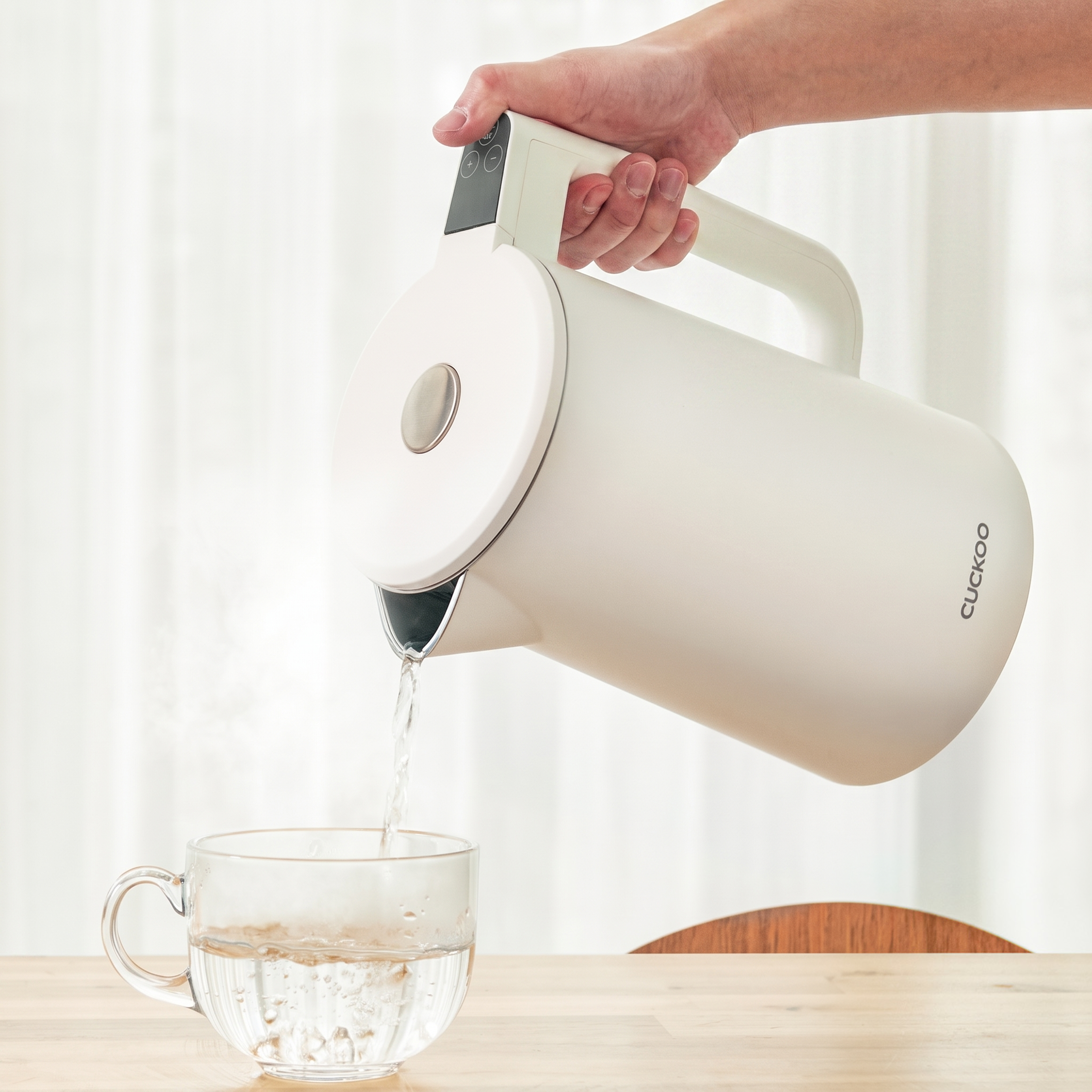 Hand pouring hot water from a white Cuckoo electric kettle into a glass cup.