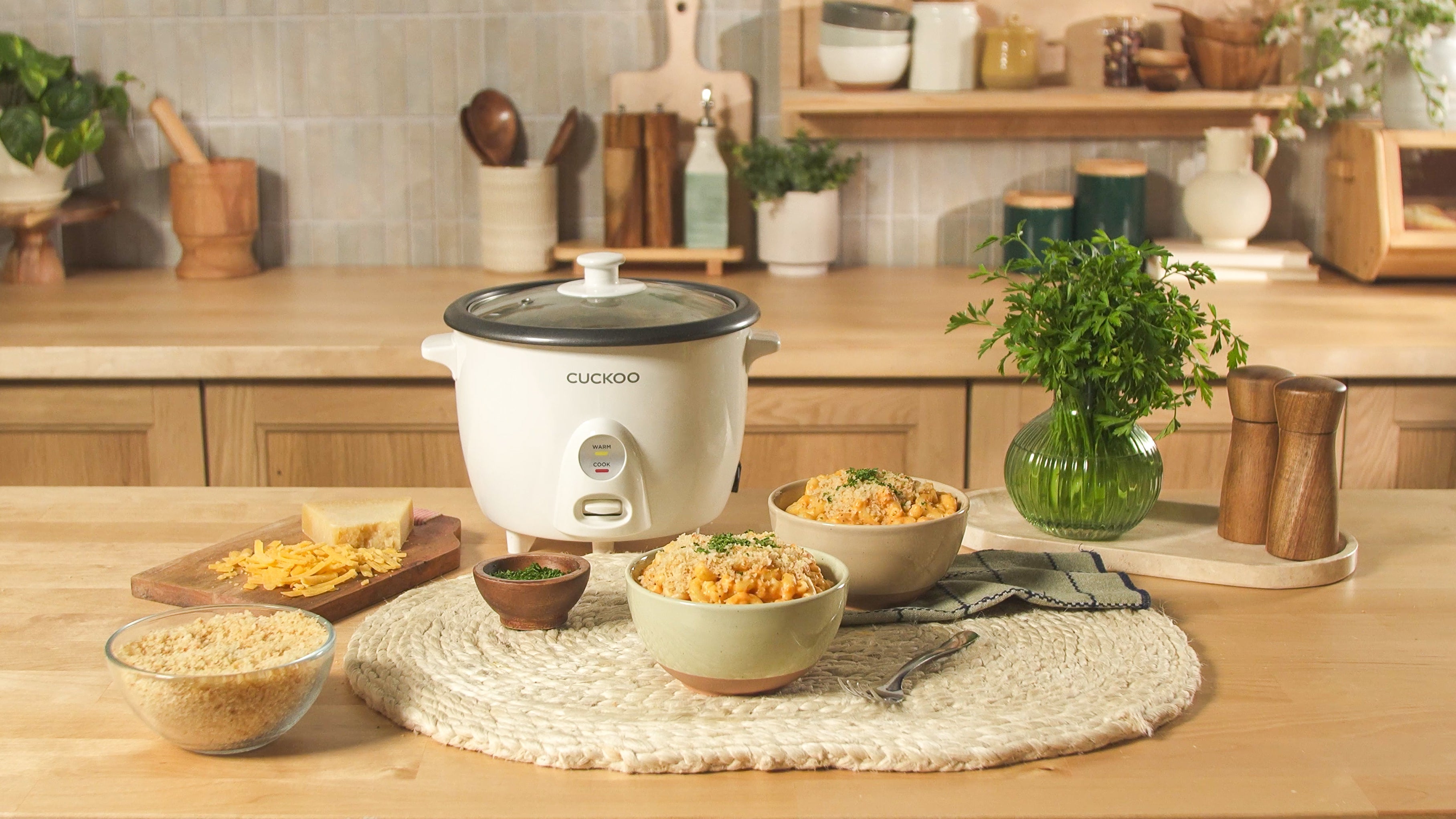 CUCKOO basic rice cooker is shown in a kitchen with 2 bowls of cooked pumpkin mac and cheese on the side.