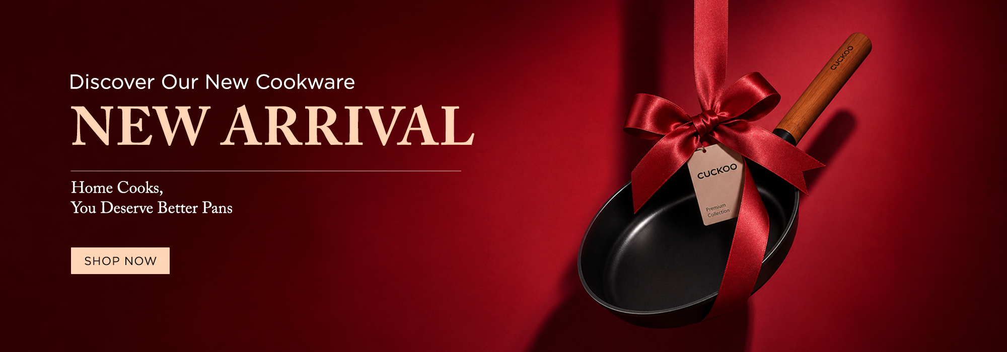 Promotional banner for a new cookware arrival featuring a black frying pan with a wooden handle tied with a red ribbon and bow, on a dark red background with text reading 'Discover Our New Cookware NEW ARRIVAL Home Cooks, You Deserve Better Panns' and a 'SHOP NOW' button.